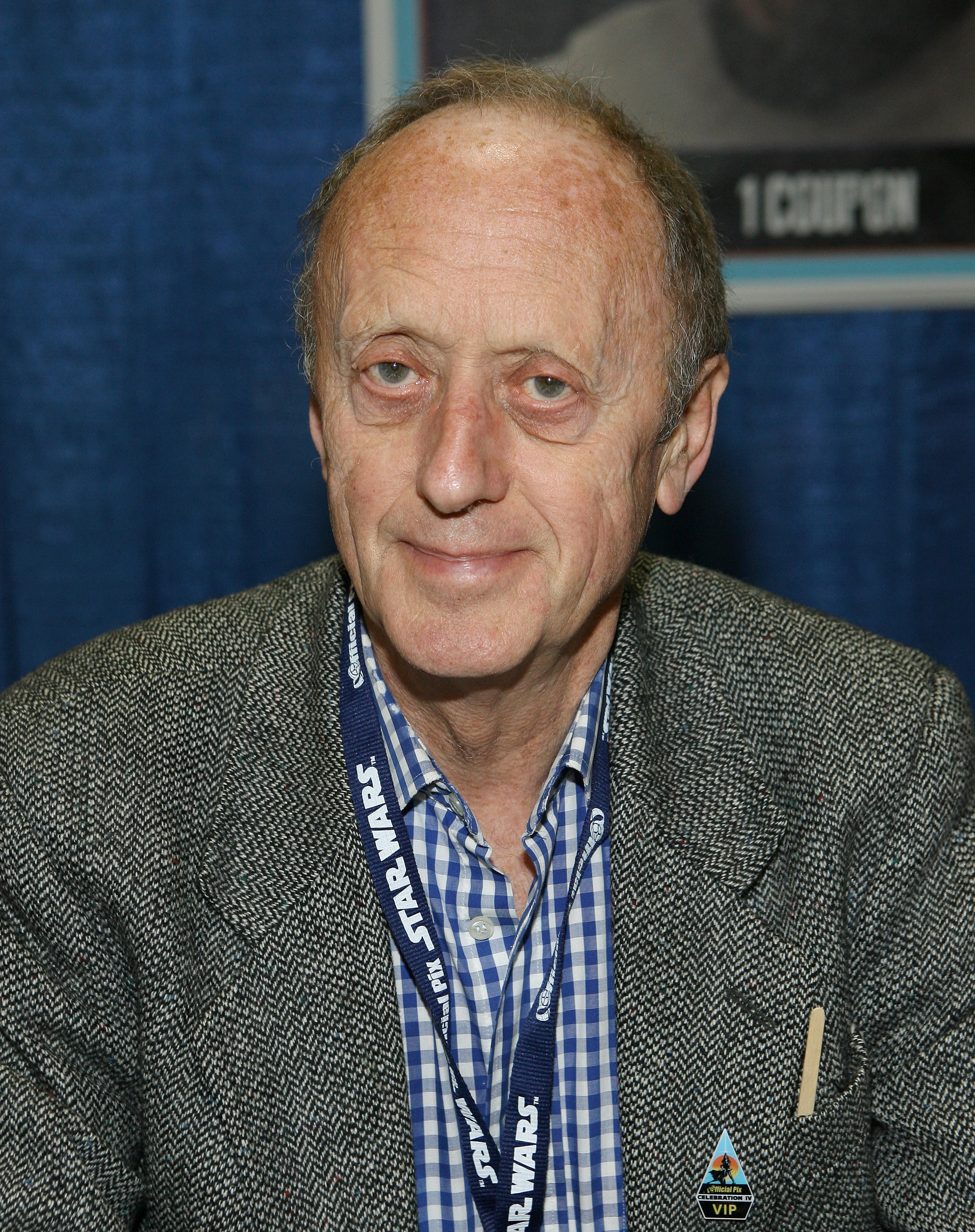 Person som deltar på et arrangement, iført en rutete skjorte og teksturert blazer, med en synlig 'Star Wars' snor rundt halsen