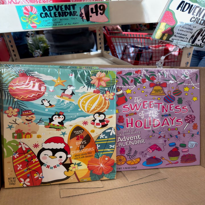 Two festive advent calendars featuring holiday-themed illustrations of penguins, ornaments, and treats displayed on a store shelf