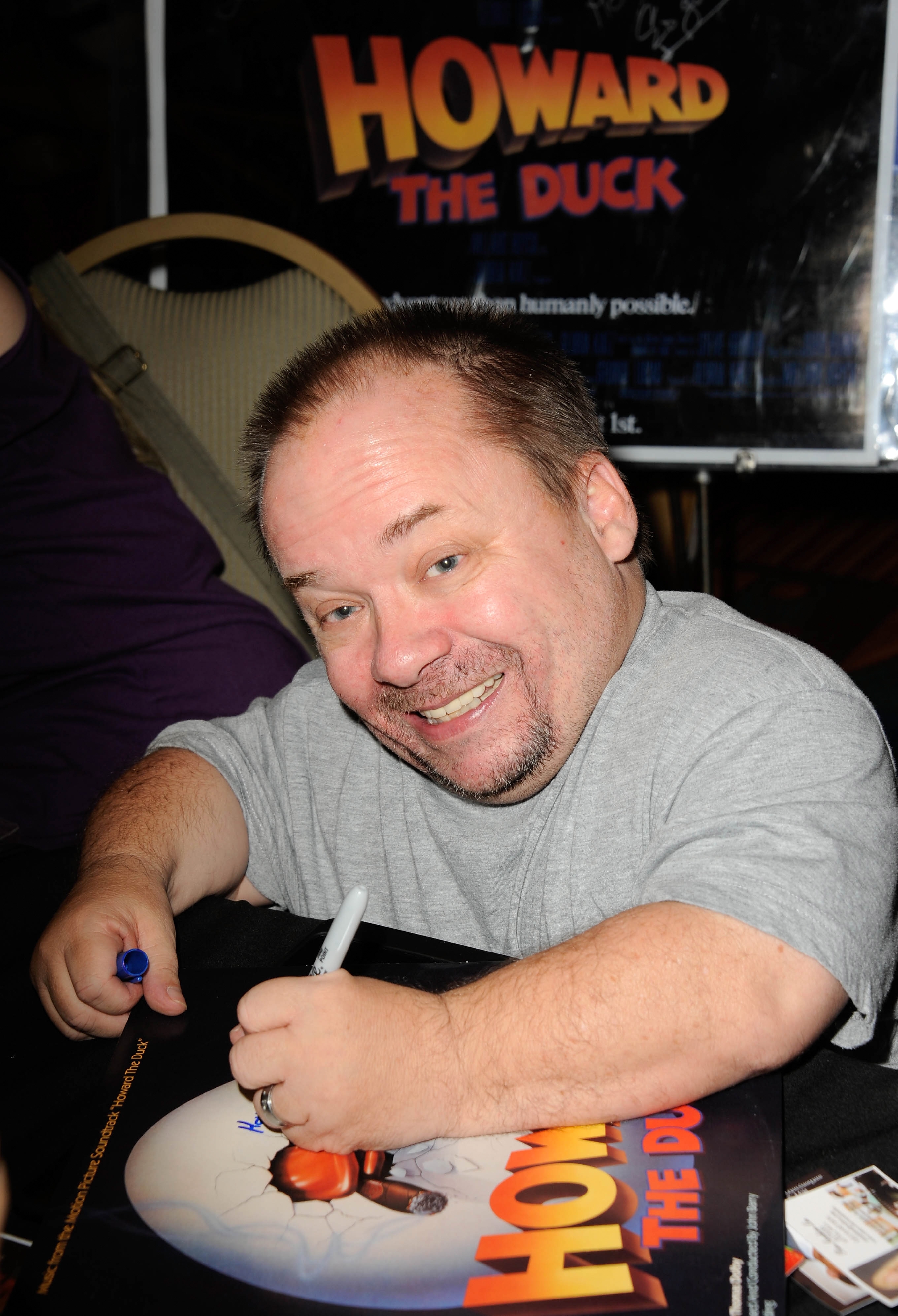 Person som smiler ved et bord og signerer en 