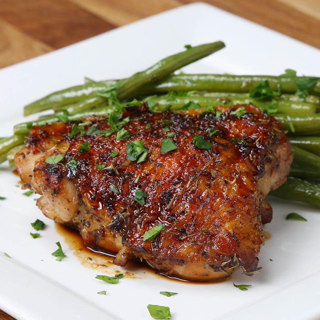 Grilled chicken thigh topped with herbs, served with green beans on a white plate