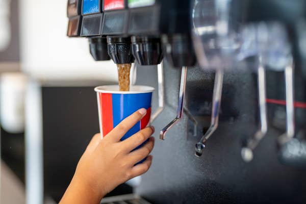 A hand fills a cup with soda from a beverage dispenser, highlighting a self-serve soda fountain in action