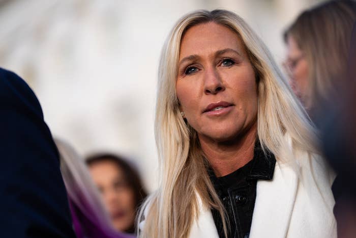 A person with long hair, wearing a white coat, looks ahead in a busy outdoor setting
