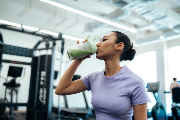 Person drinking a green smoothie in a gym setting, wearing athletic wear, highlighting a fitness lifestyle