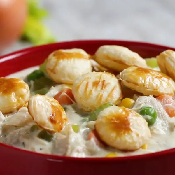 Hearty chicken pot pie soup topped with flaky biscuits in a red bowl