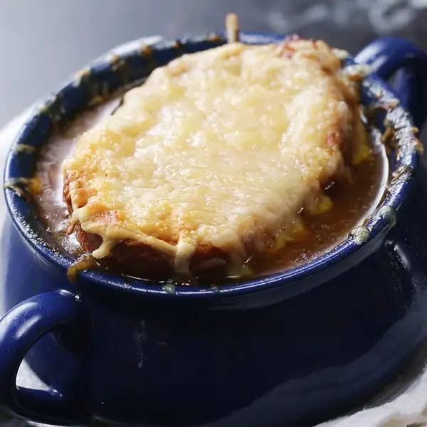 Bowl of French onion soup topped with melted cheese over a slice of bread, in a blue ceramic serving dish