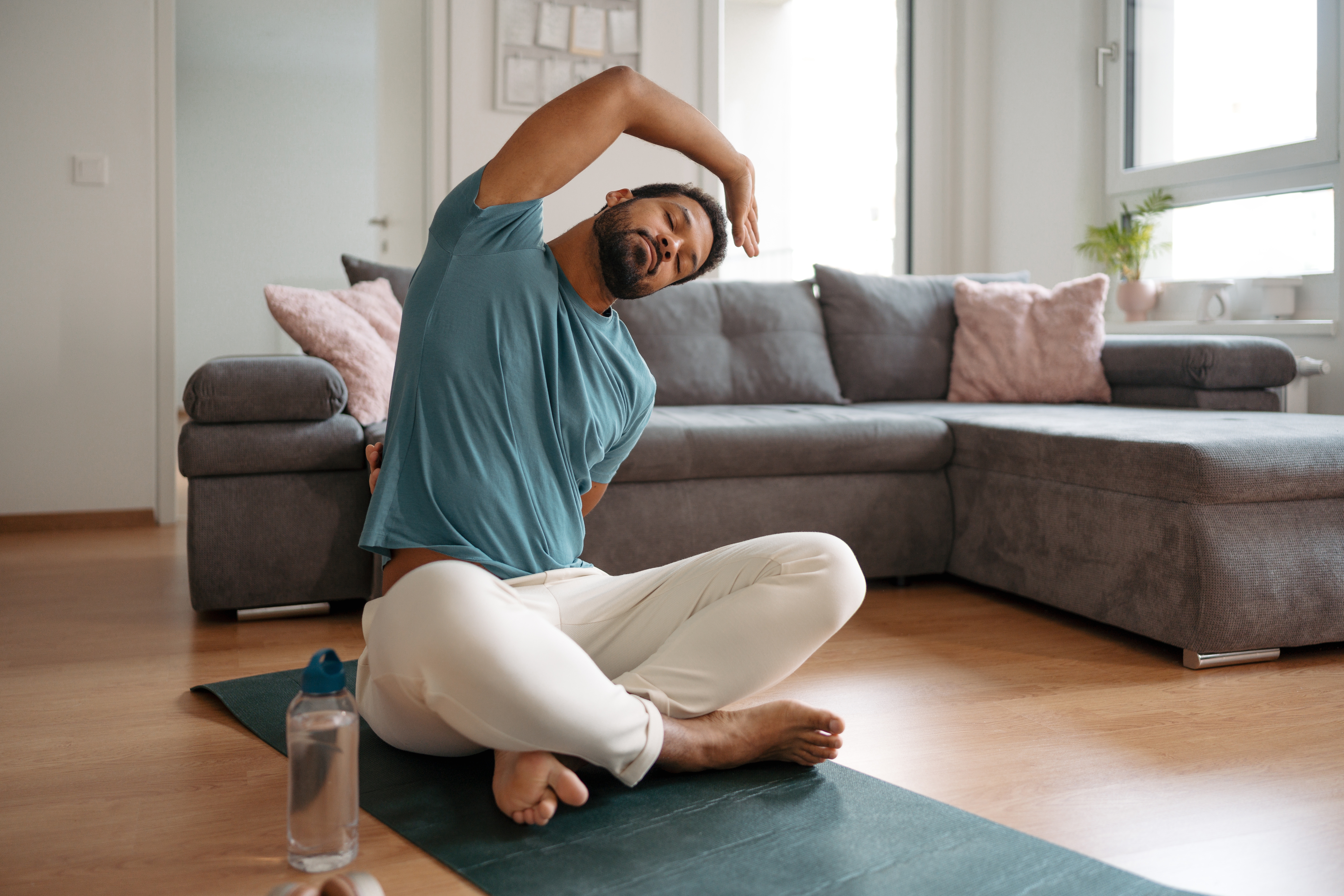 A antheral practices yoga astatine home, seated connected a mat adjacent to a h2o bottle