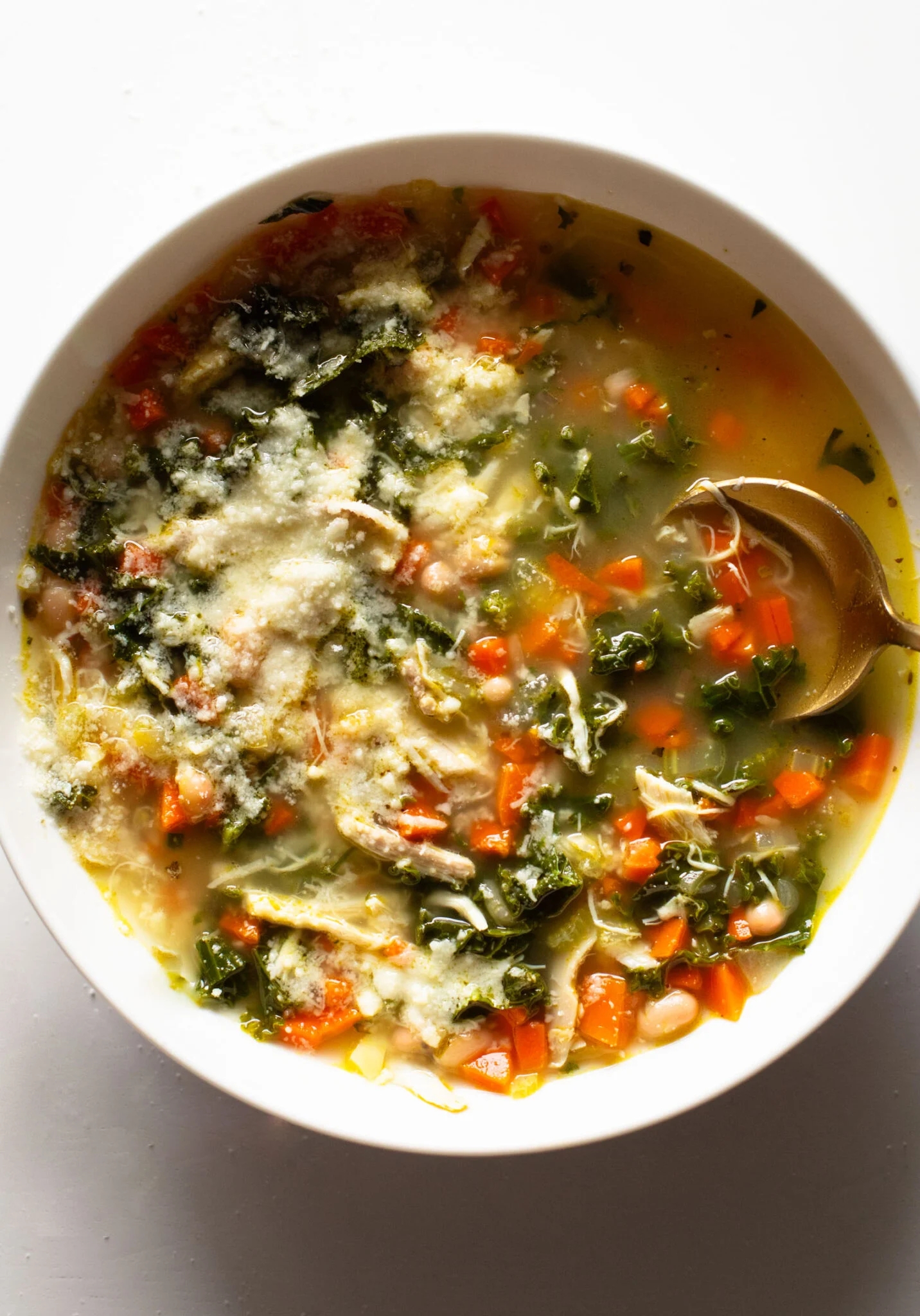 Bowl of hearty soup with vegetables, beans, shredded greens, and sprinkled cheese on top, with a spoon resting inside