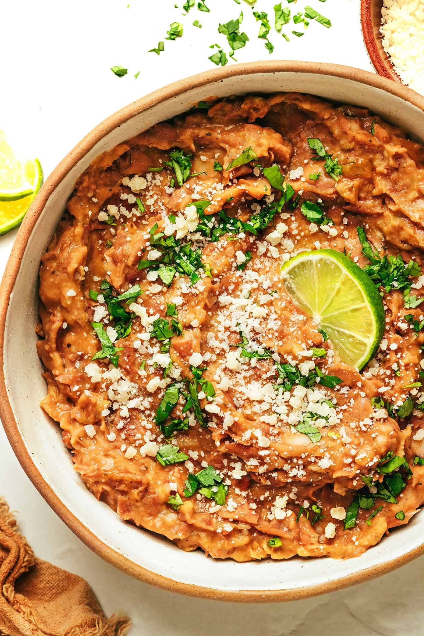 A bowl of refried beans topped with crumbled cheese, chopped cilantro, and a lime wedge