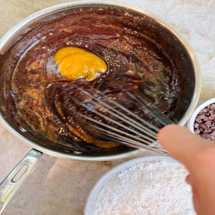 Whisking an egg into a pot of chocolate batter, with bowls of flour and chocolate chips nearby