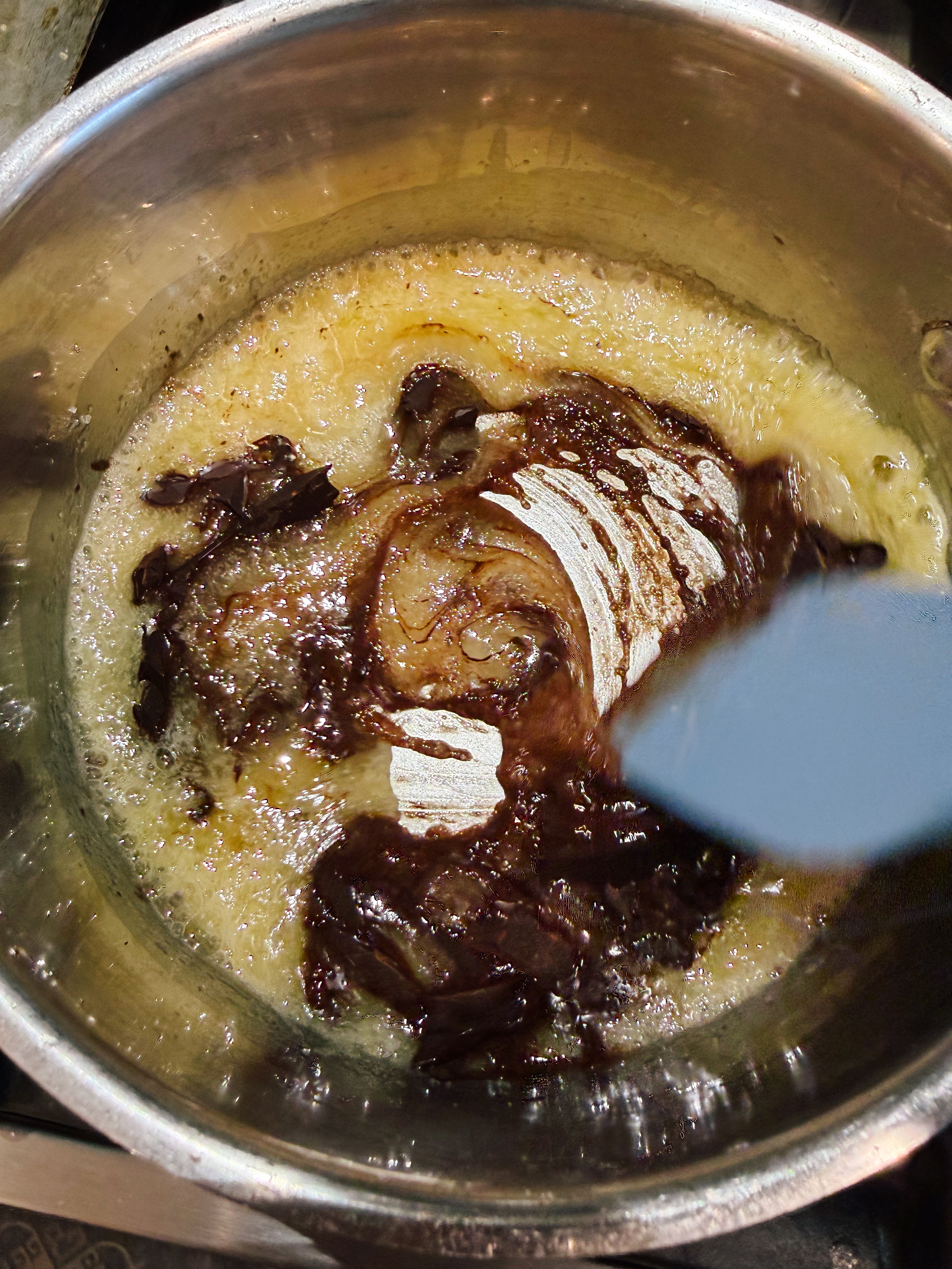 A stew of caramelized onions, garlic, and sugar in a pot, being stirred with a spatula