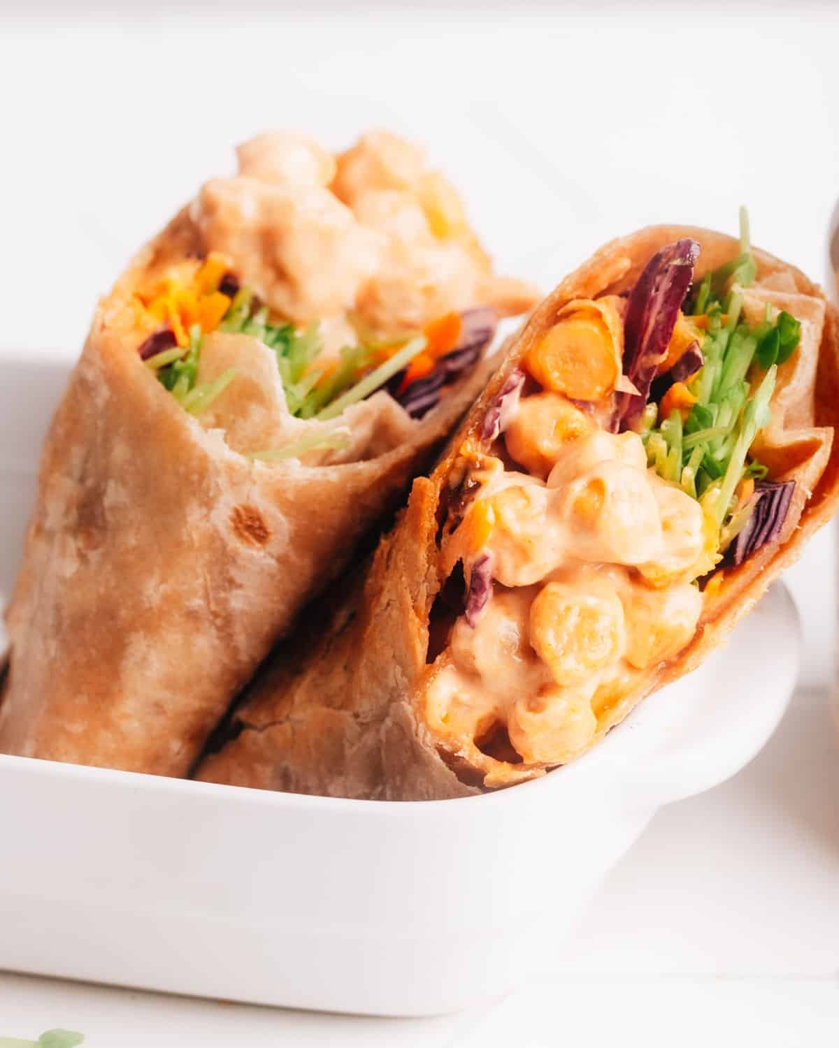 Close-up of two wraps filled with chickpeas, greens, and shredded carrots in a white dish
