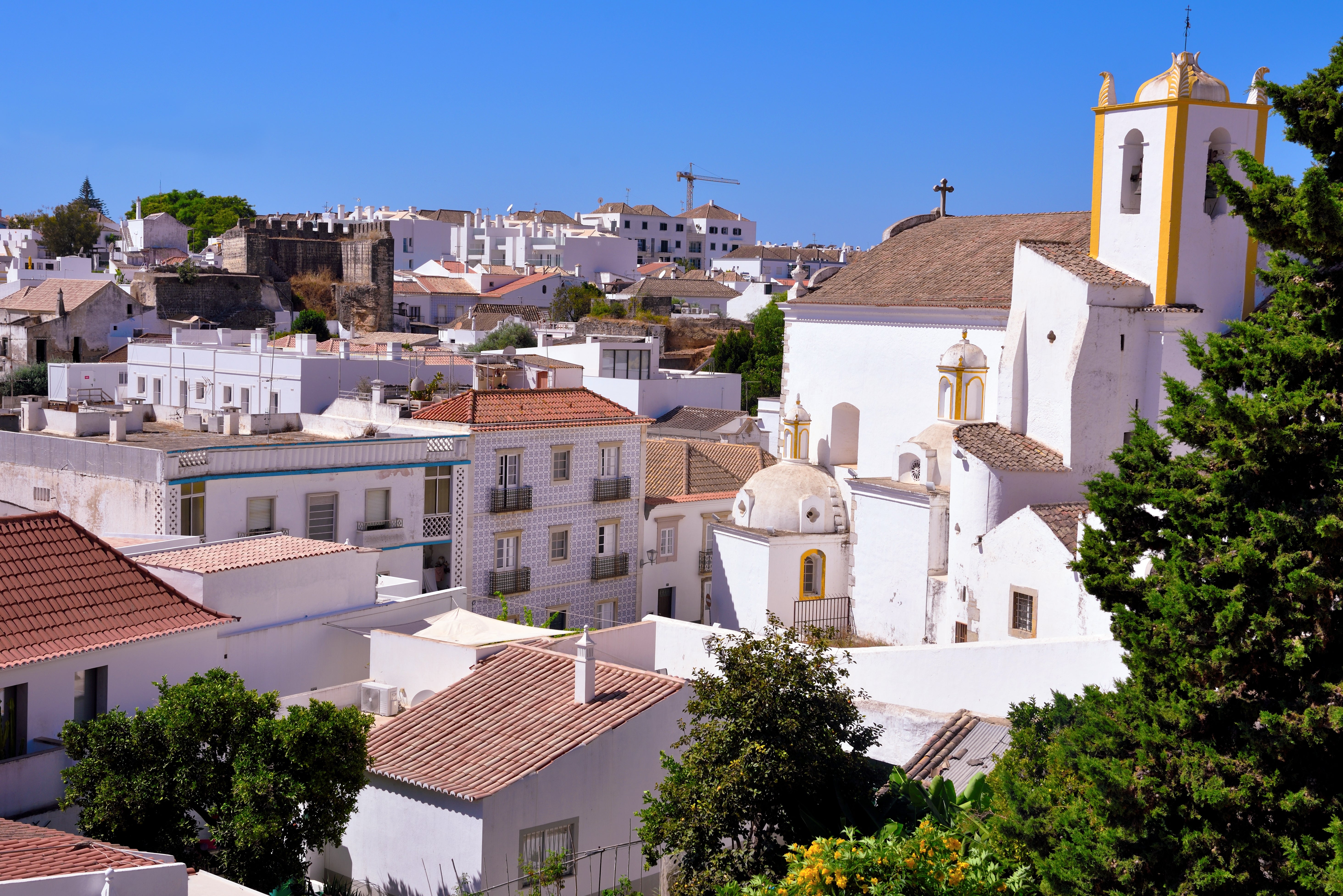 Scenic view of a historic town with white buildings and a church, surrounded by greenery, under a clear sky