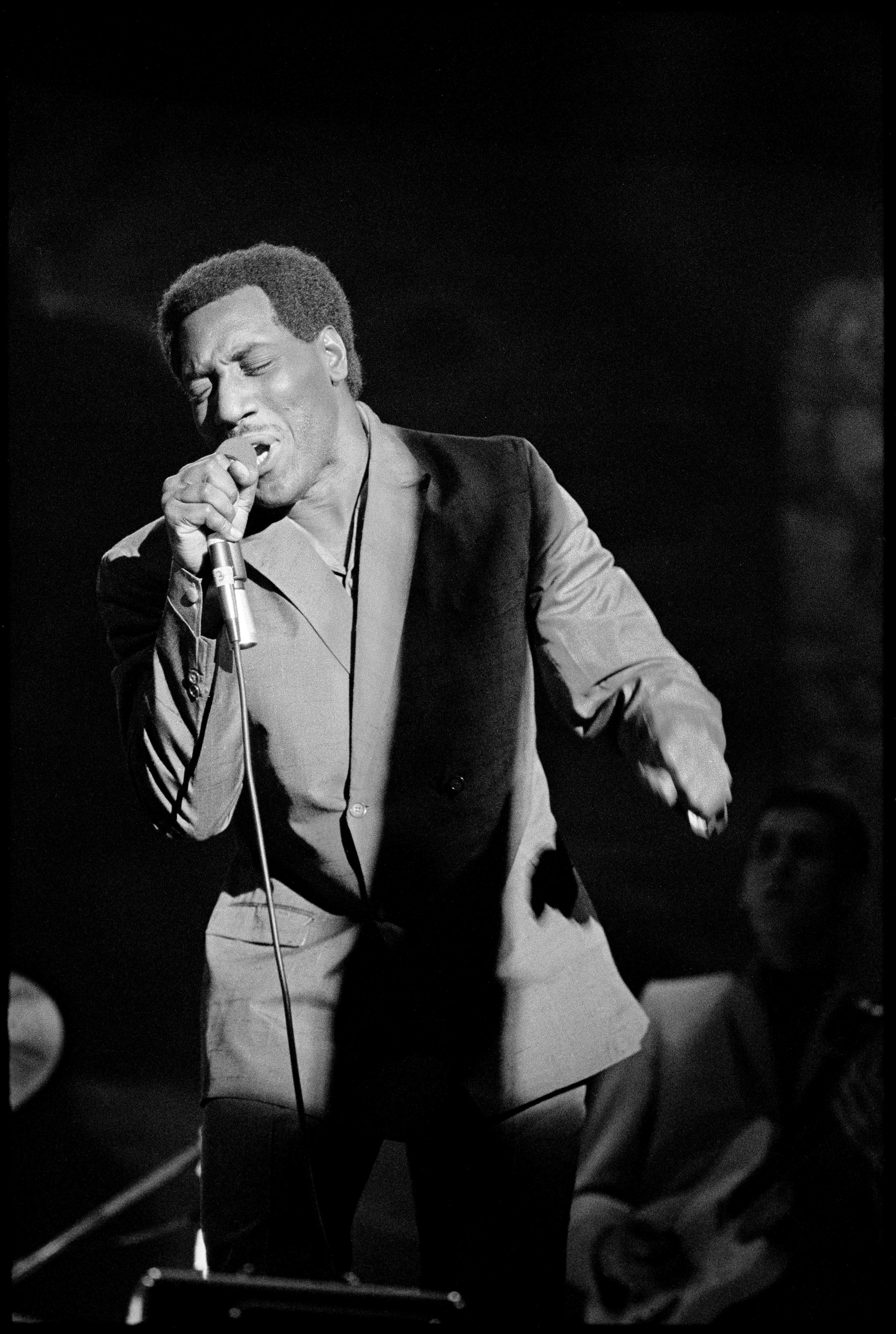 A instrumentalist  passionately sings into a microphone connected  stage, wearing a suit. A set  subordinate   is disposable   successful  the background