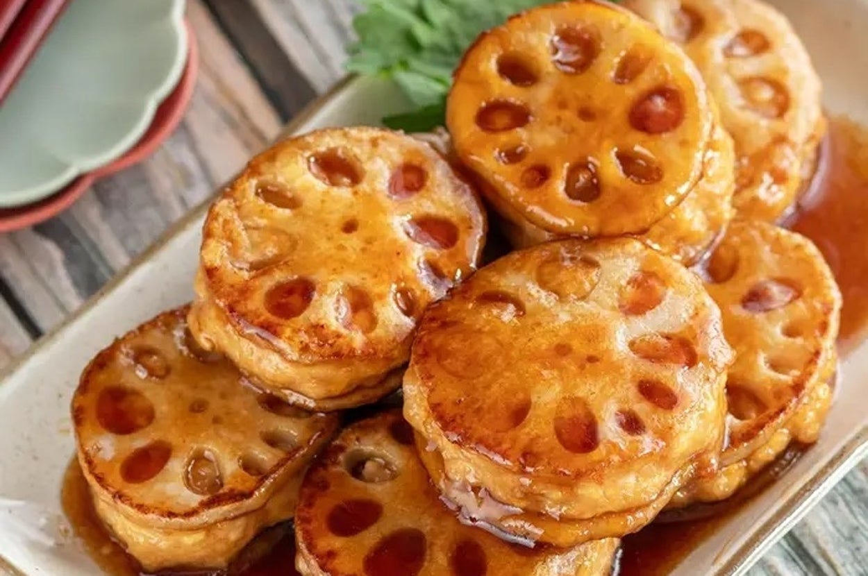 レンコンの甘辛煮が皿に盛られています。照りのあるソースで、付け合わせに緑の葉が添えられています。