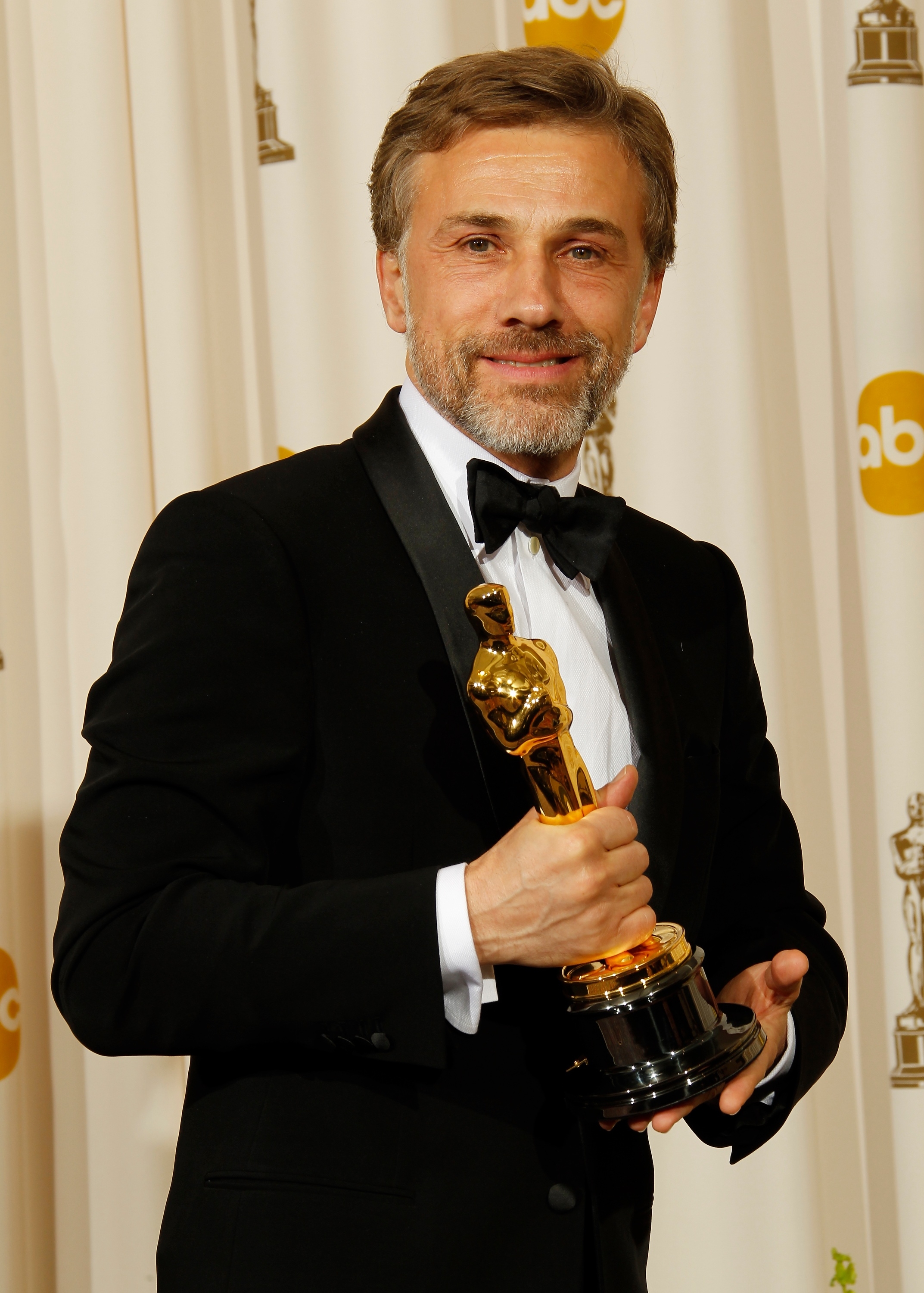 Person successful  a tuxedo holding an grant  statue, smiling astatine  an event