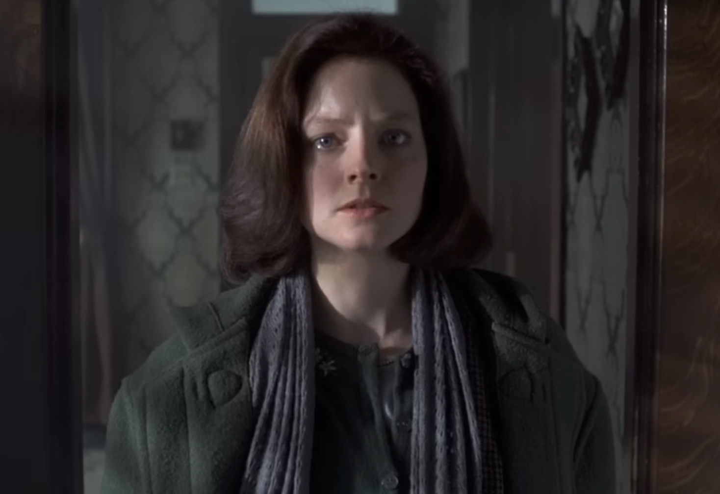 Person looking serious, wearing a overgarment  and scarf, stands successful  a dimly lit room