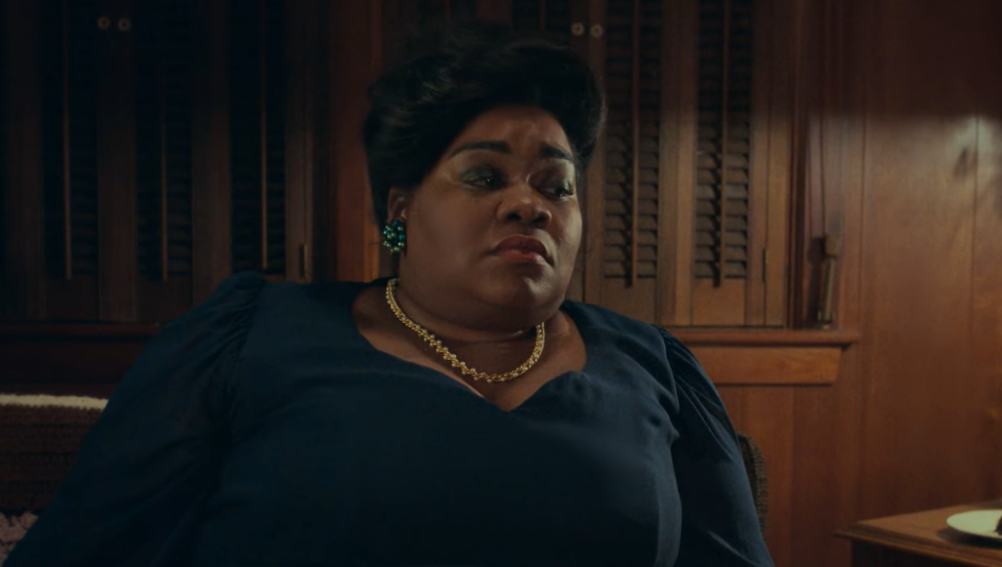 Person successful  a acheronian  outfit with puffed sleeves, wearing a golden  necklace and earrings, seated successful  a dimly lit room