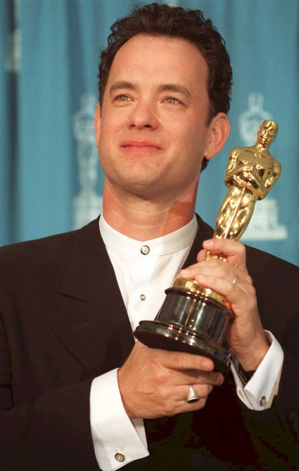 Person successful  a tuxedo holding an Oscar statuette, smiling, lasting  against a bluish  backdrop