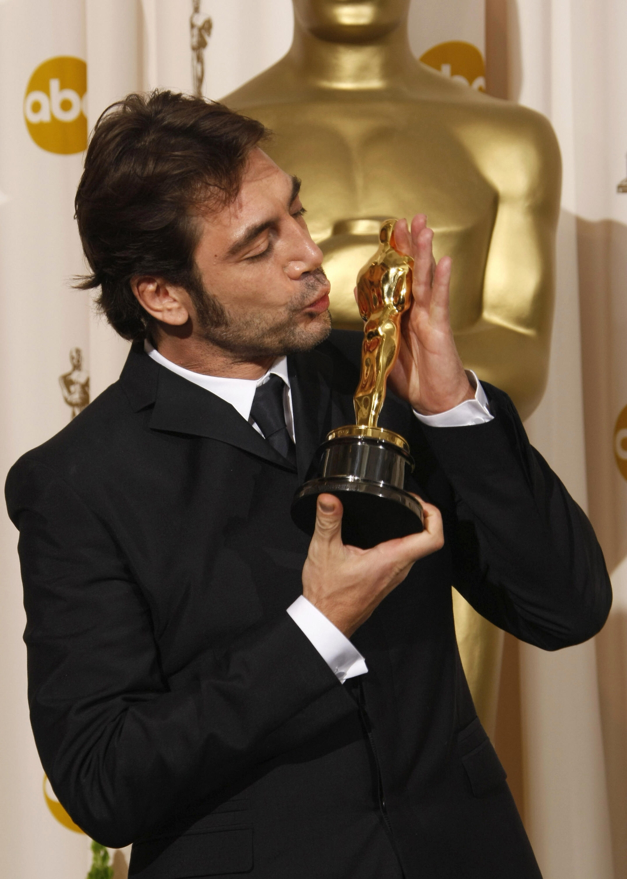 Person successful  a suit   kisses an grant  statue successful  beforehand   of a backdrop with golden  statuettes