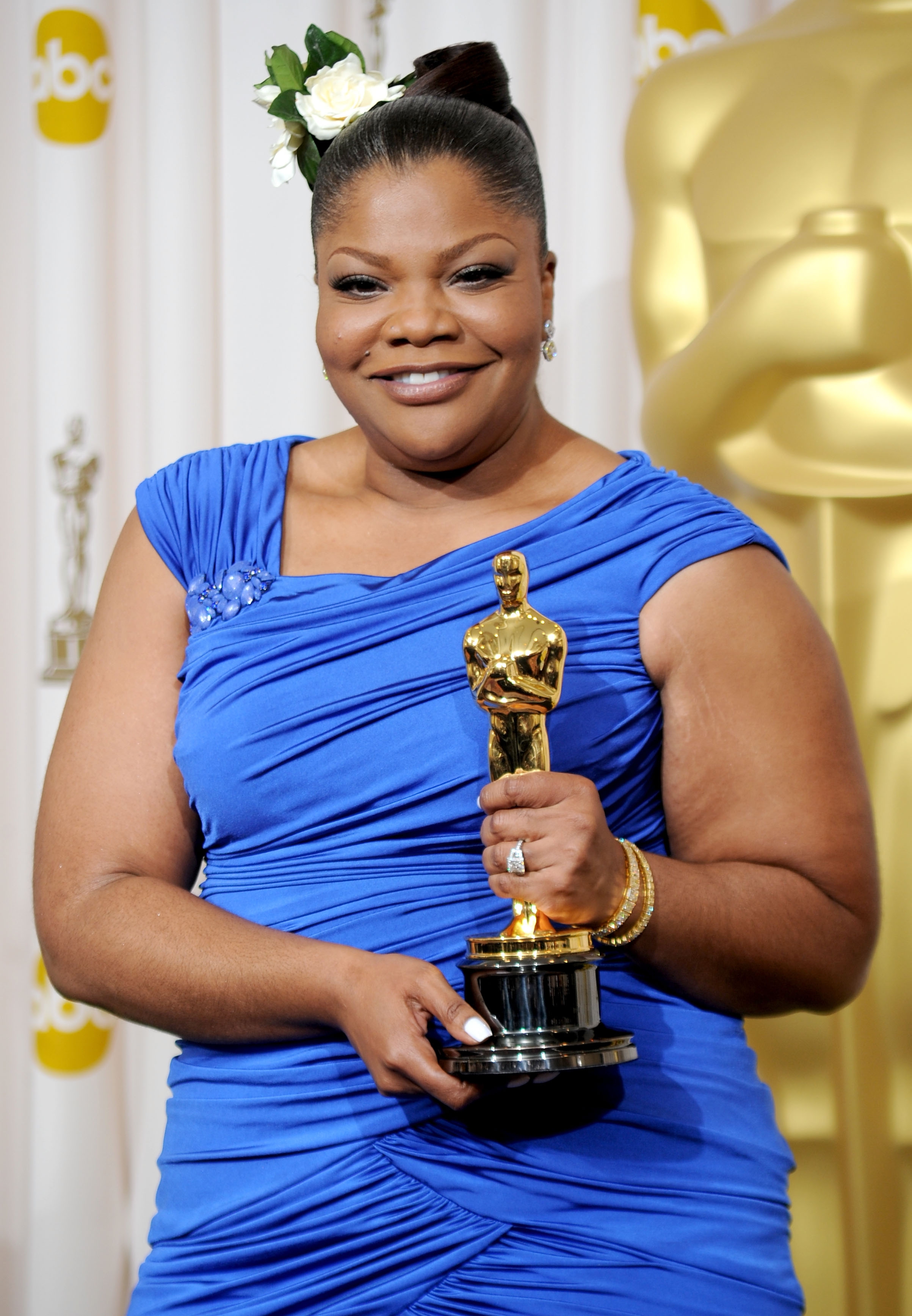 Person successful  elegant bluish  gown holds an Oscar trophy, smiling successful  beforehand   of a backdrop with award-themed decor