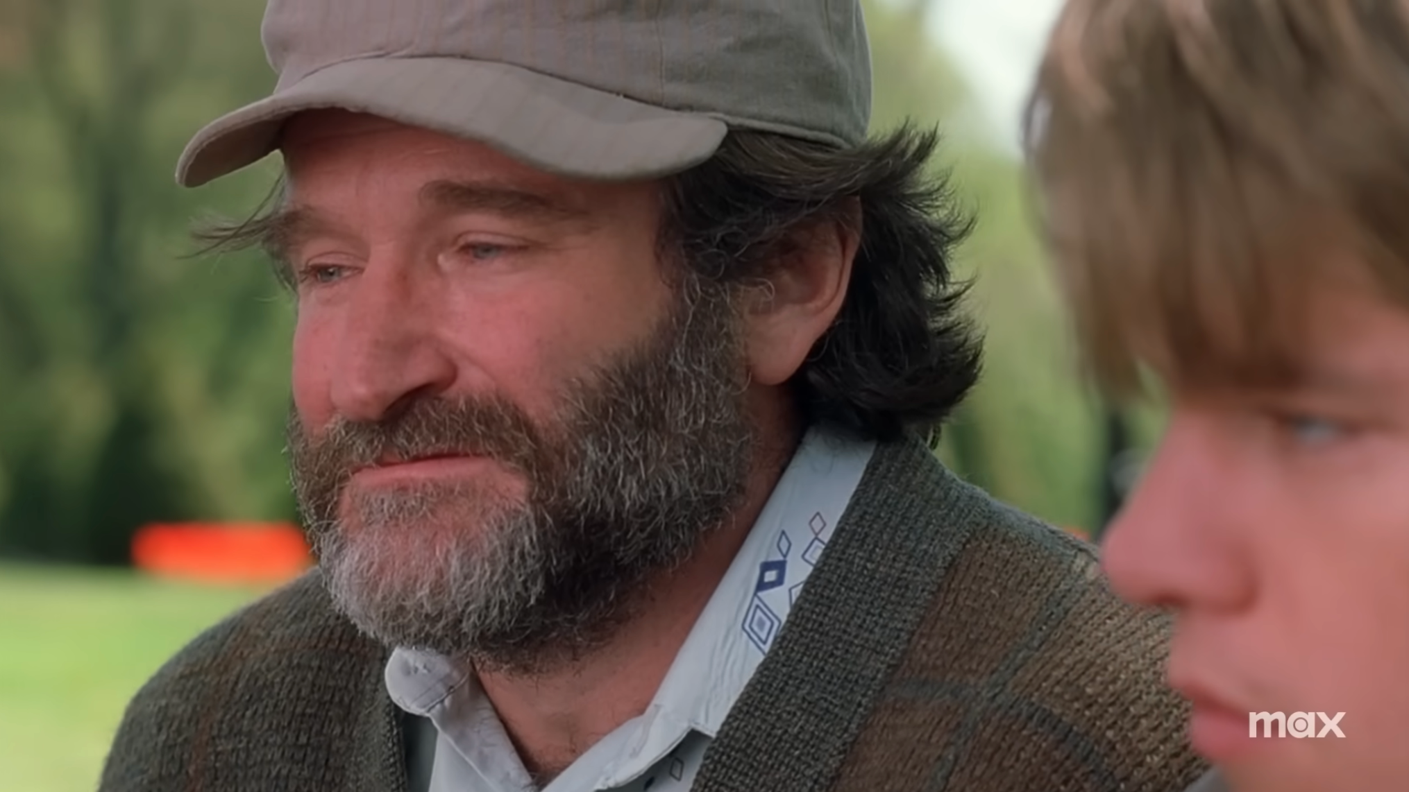 Two radical   sitting outdoors, 1  wearing a headdress  and sweater, with a thoughtful expression