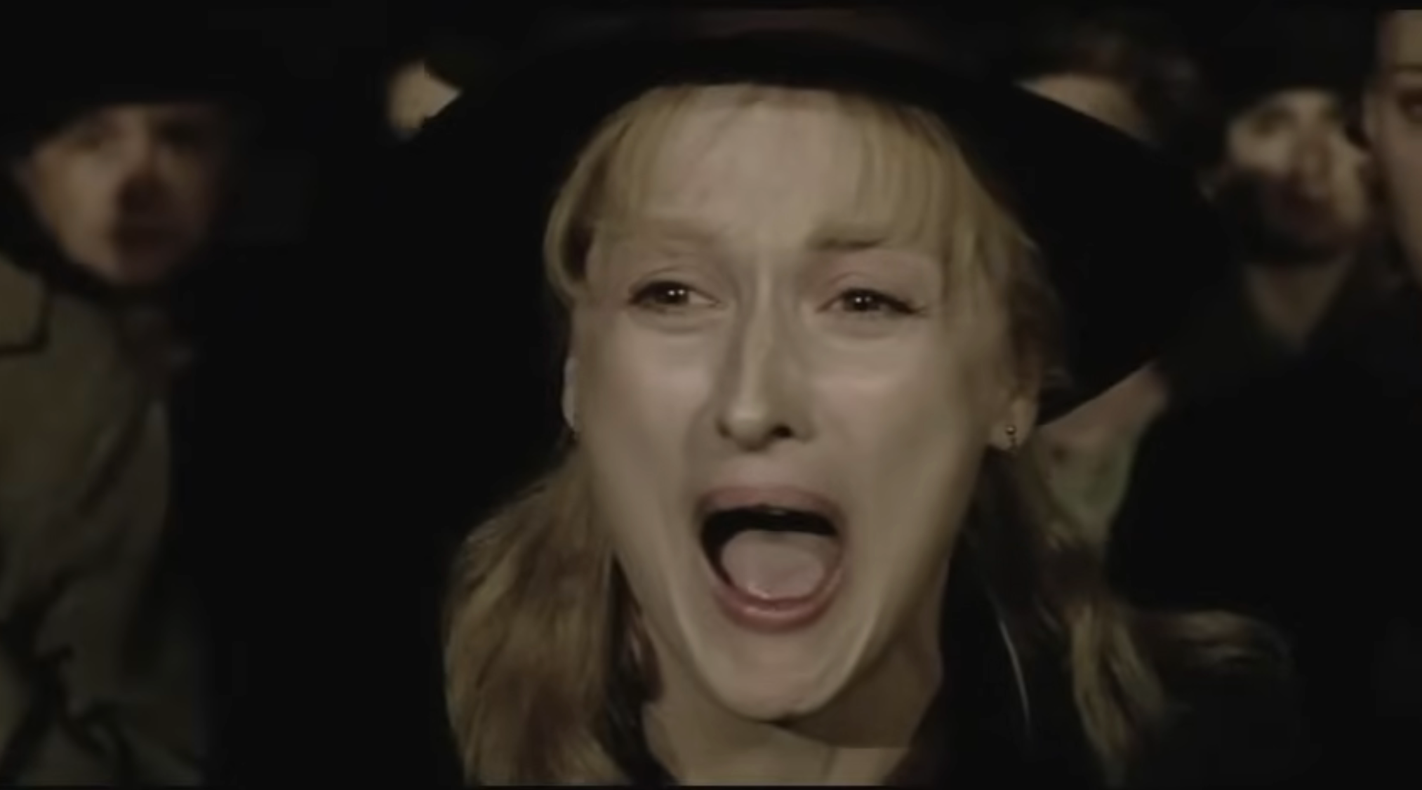 A idiosyncratic   successful  a movie   country   appears distressed, rima  unfastened  successful  a shout, wearing a hat, with others successful  the blurred background