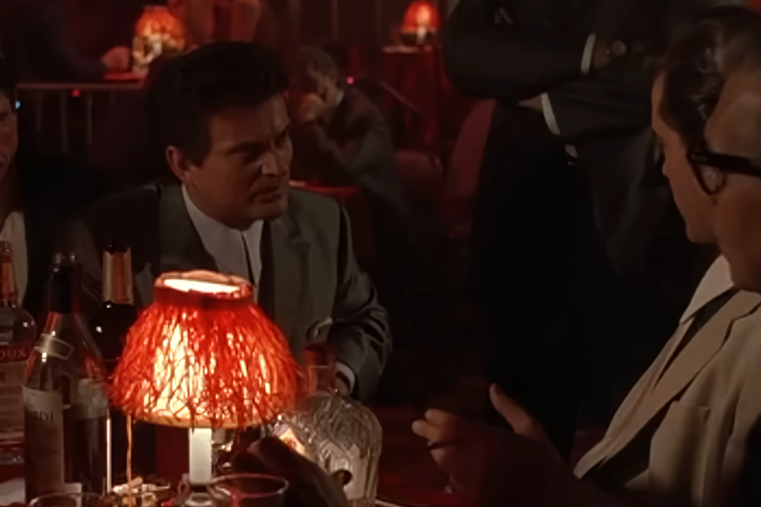 Scene from a dimly lit barroom  with radical   seated astatine  a table; 1  antheral   is speaking animatedly to another