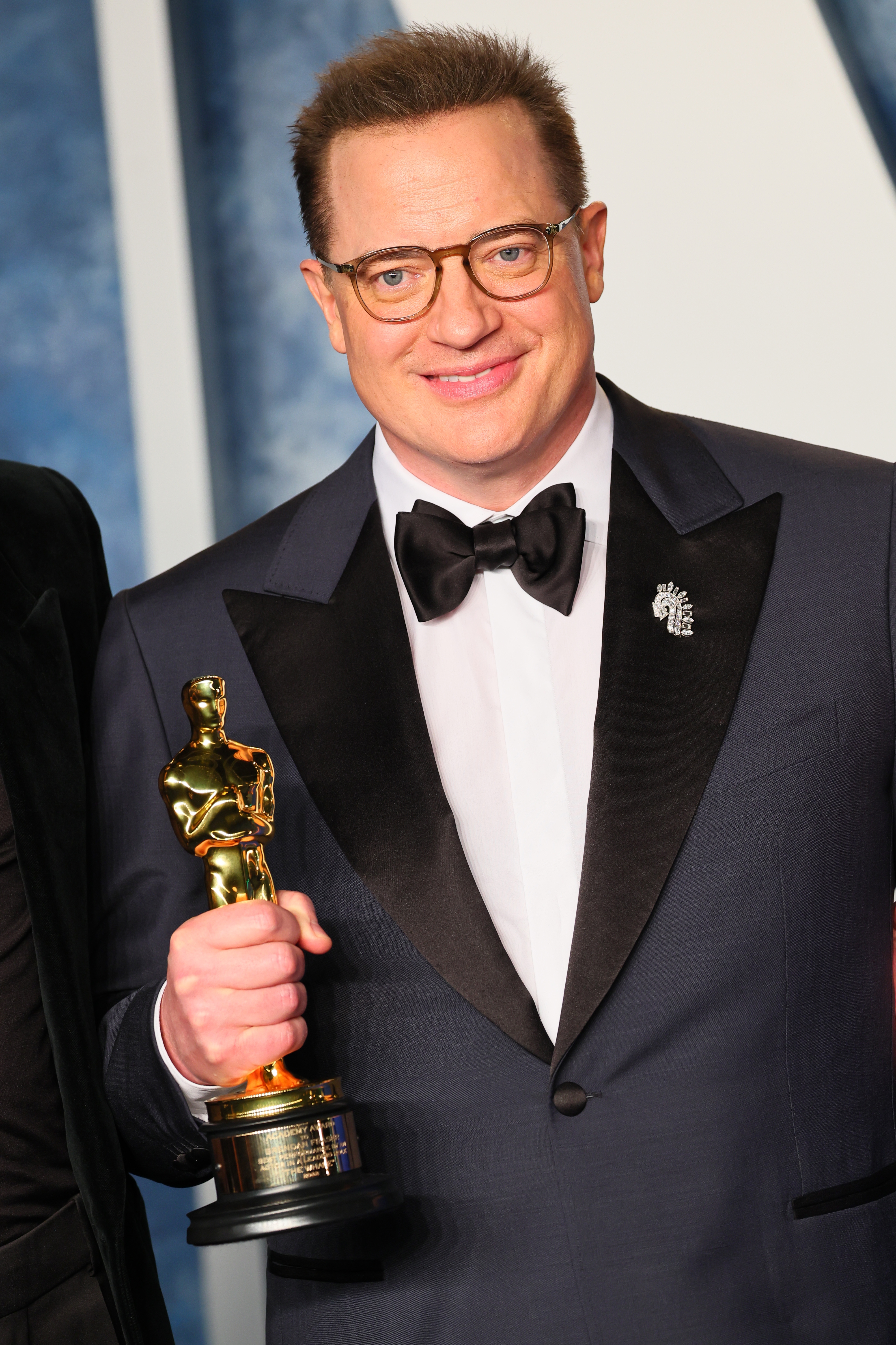 Person successful  a tuxedo holds an grant  statue, smiling astatine  an event