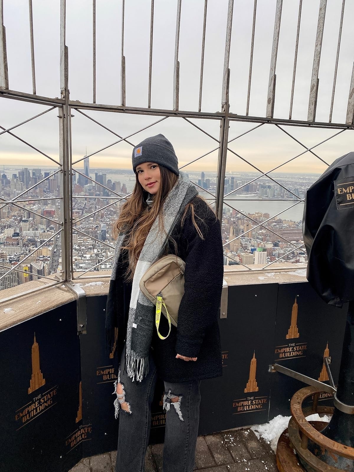 Person successful  wintertime  attire stands connected  Empire State Building reflection  deck, holding a beige purse, with metropolis  skyline successful  the background