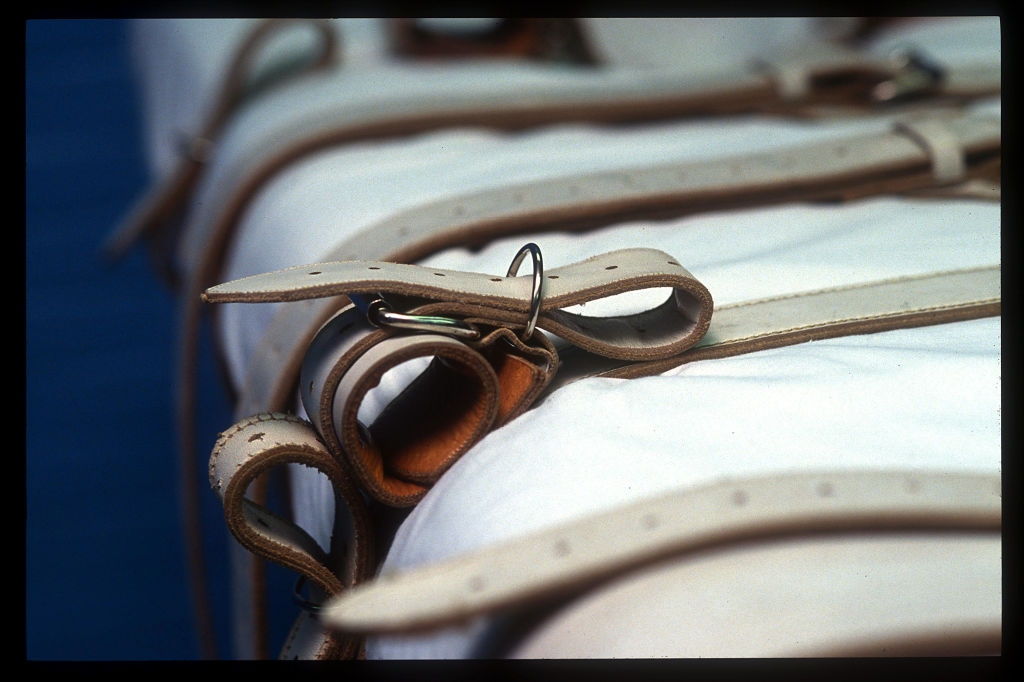 Close-up view of straps and buckles on a white mattress, suggesting restraint or confinement