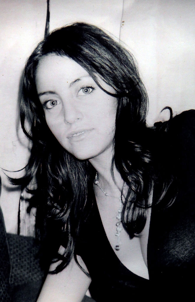A woman with long hair and a necklace is posing for a photo, gazing at the camera