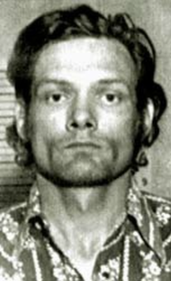 A serious-faced individual in a patterned shirt faces the camera for a portrait-style image