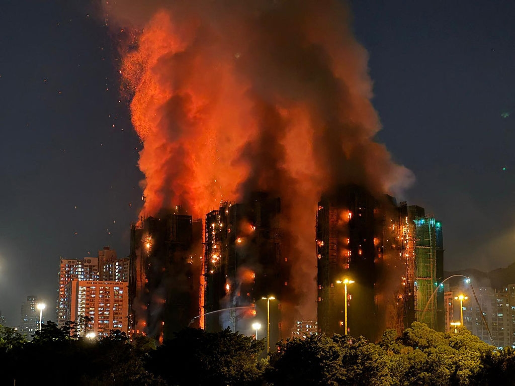 Large building engulfed in flames at night, with smoke and sparks rising into the sky, illuminating the surrounding area