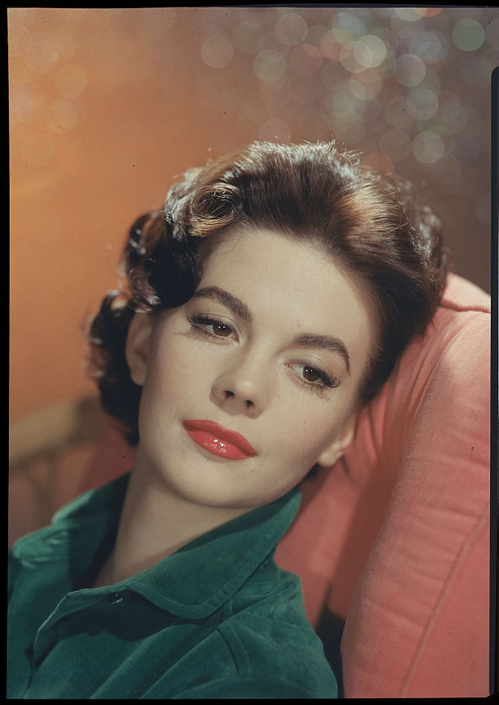 Person with elegant hairstyle, wearing a stylish blouse, poses with a serene expression