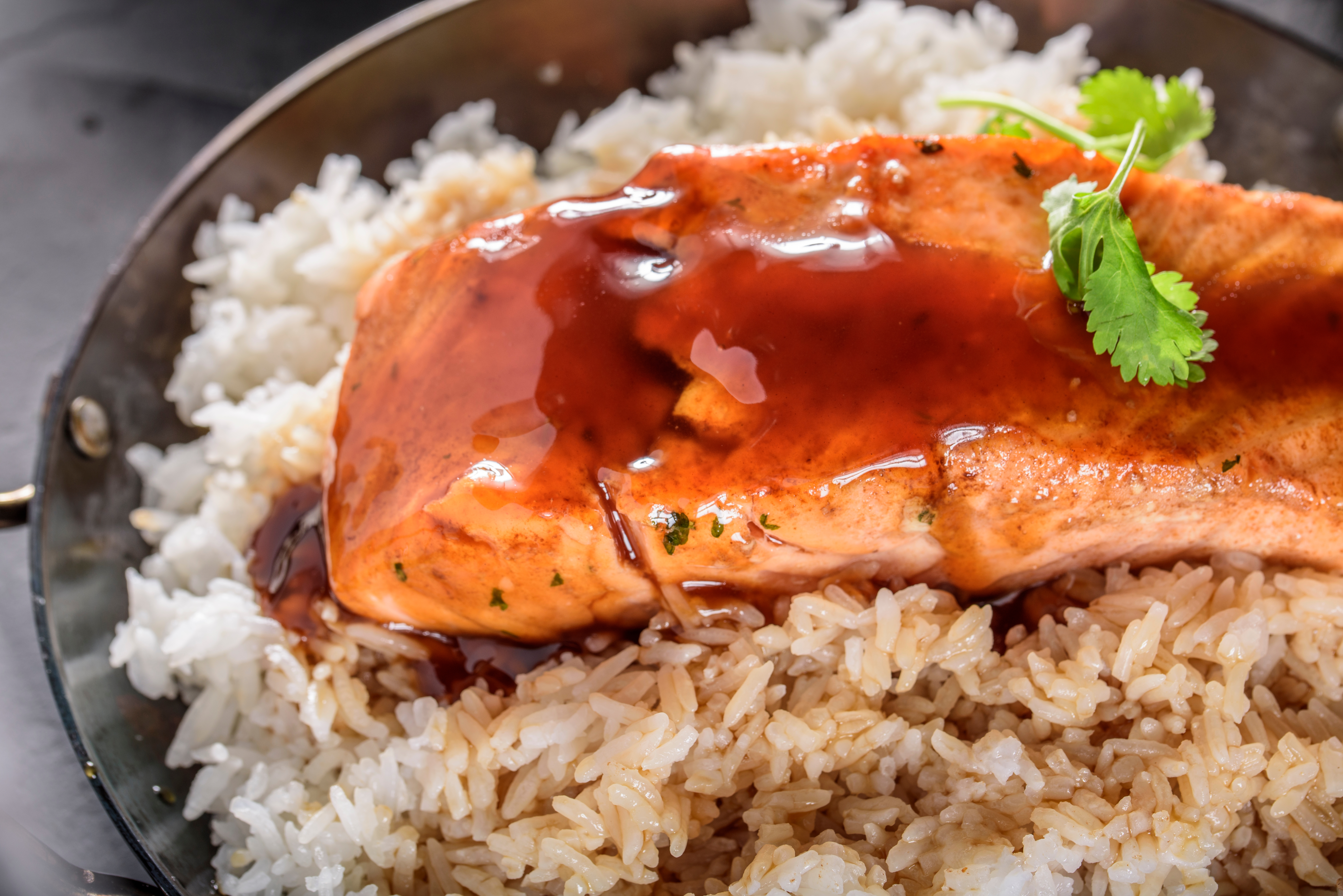 Salmon glazed with sauce on a bed of rice, garnished with cilantro, served in a metal dish
