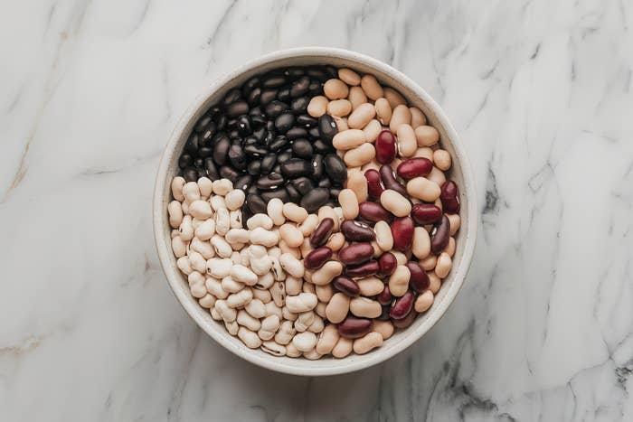 A round bowl holds an assortment of beans, including black, white, and red, arranged in sections on a marble surface
