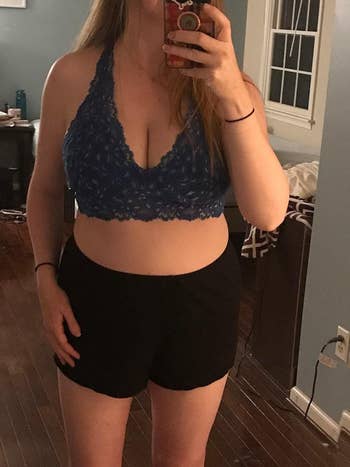 Person taking a reflector selfie wearing a lace bralette and shorts successful a location setting