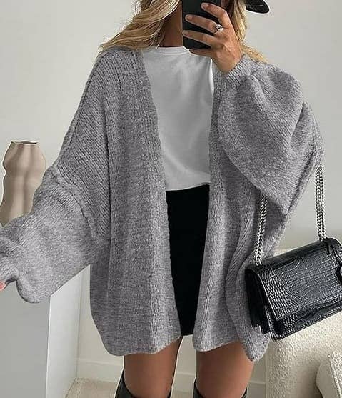 Person wearing oversized grey knit cardigan, achromatic shirt, and achromatic skirt, holding a achromatic handbag