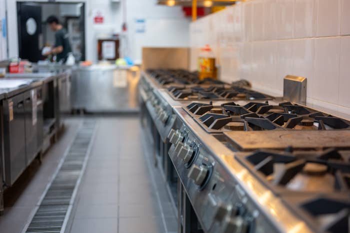Commercial kitchen with multiple stove burners lined up, blurred figure working in the background