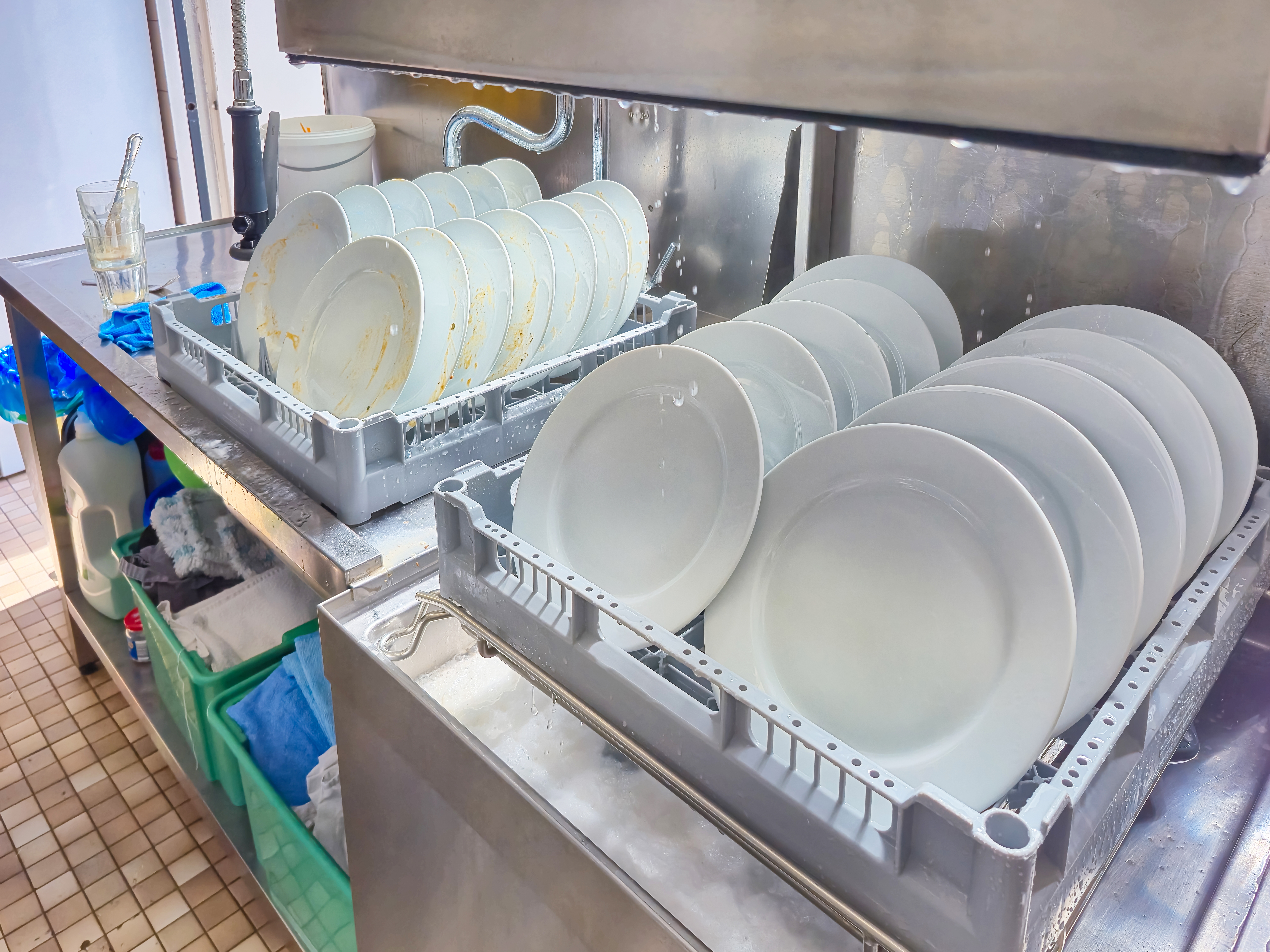 Dishes are stacked in a commercial dishwasher, with some visibly dirty and others clean, in a kitchen setting