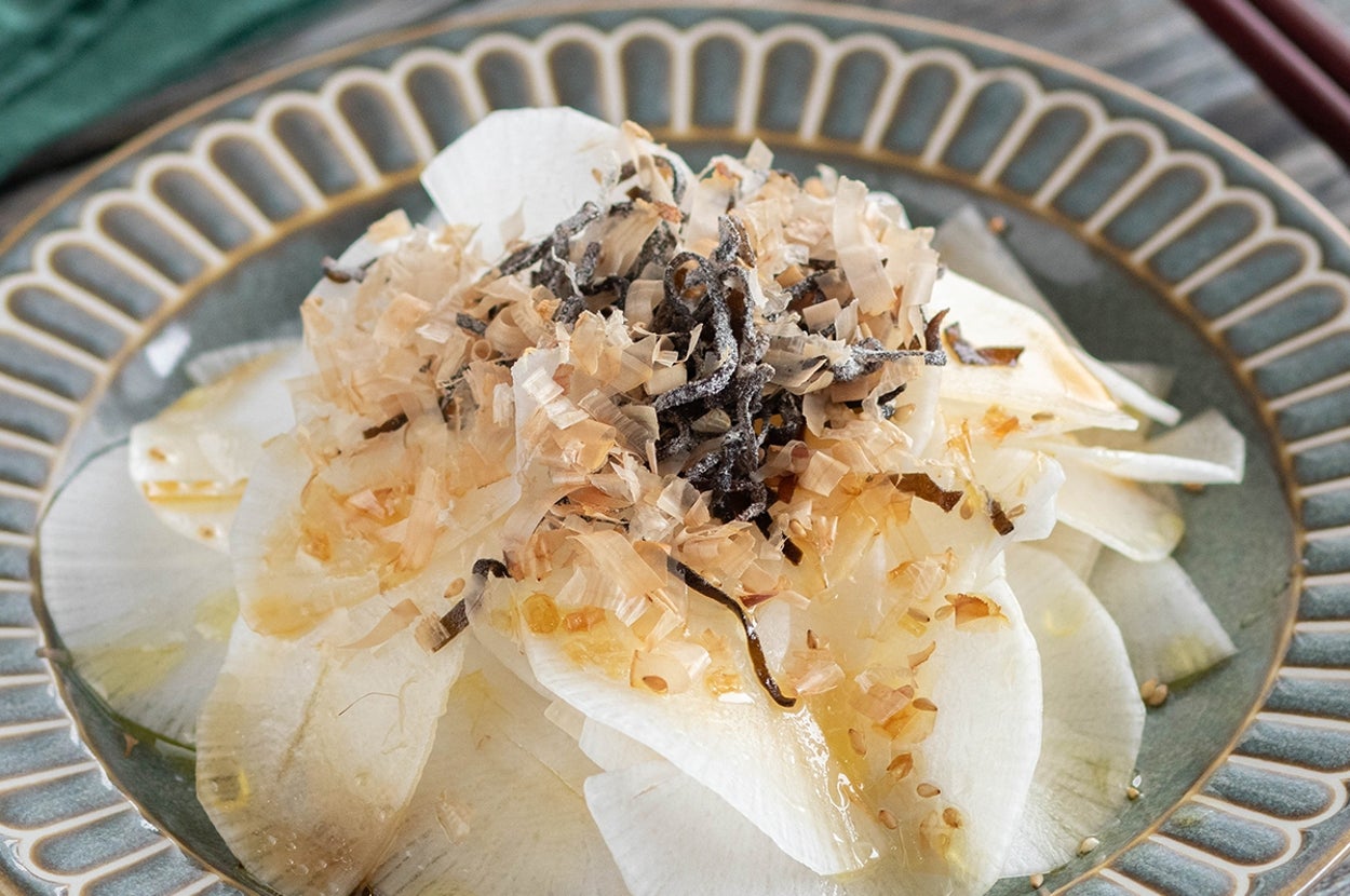 大根の薄切りに削り節と海藻が載った和風サラダが陶製の皿に盛られている。箸が横に置かれている。