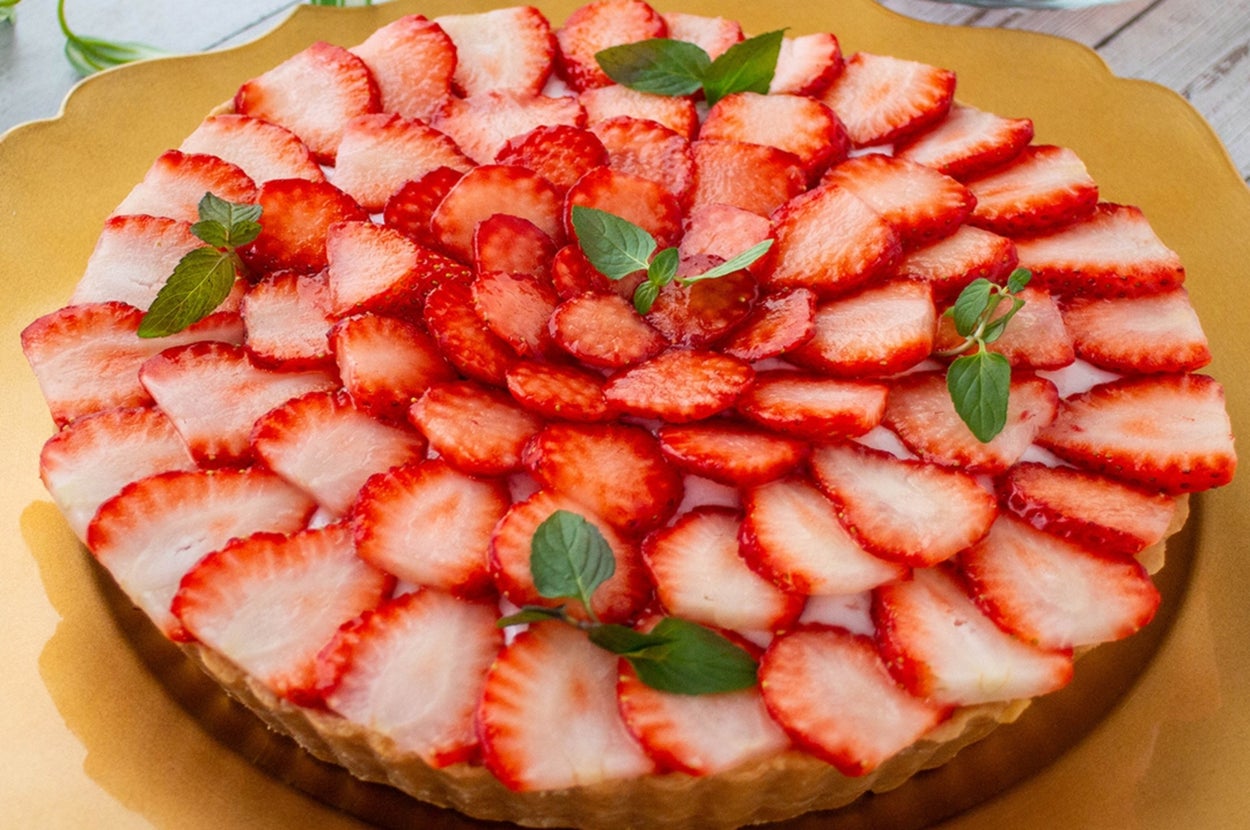 いちごのスライスで飾られたタルトがゴールドのプレートに載せられている。ティーカップも後ろに見える。