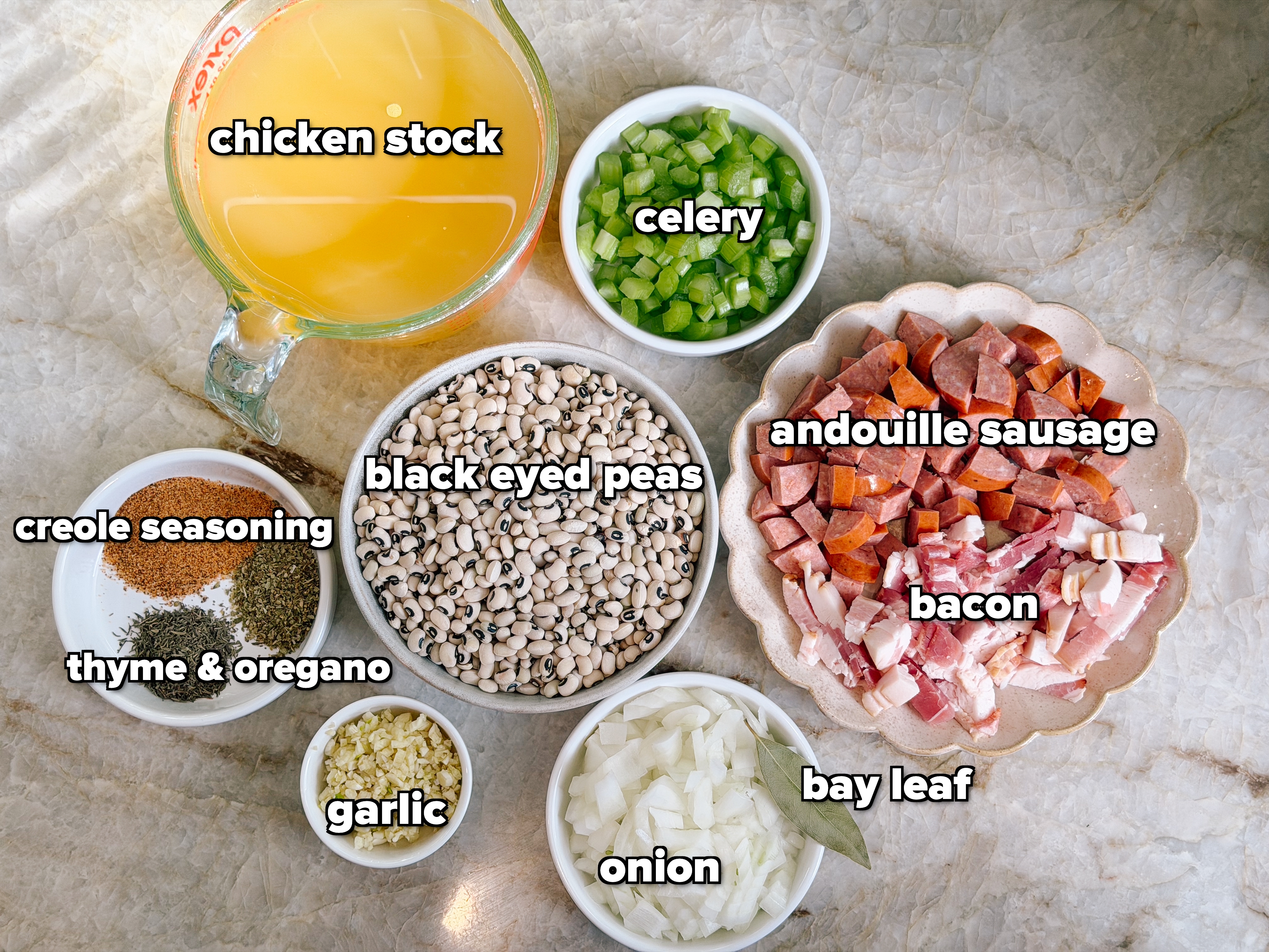 Ingredients for a recipe neatly arranged: chopped bacon, sausages, diced onions, green peppers, black-eyed peas, spices, minced garlic, and broth