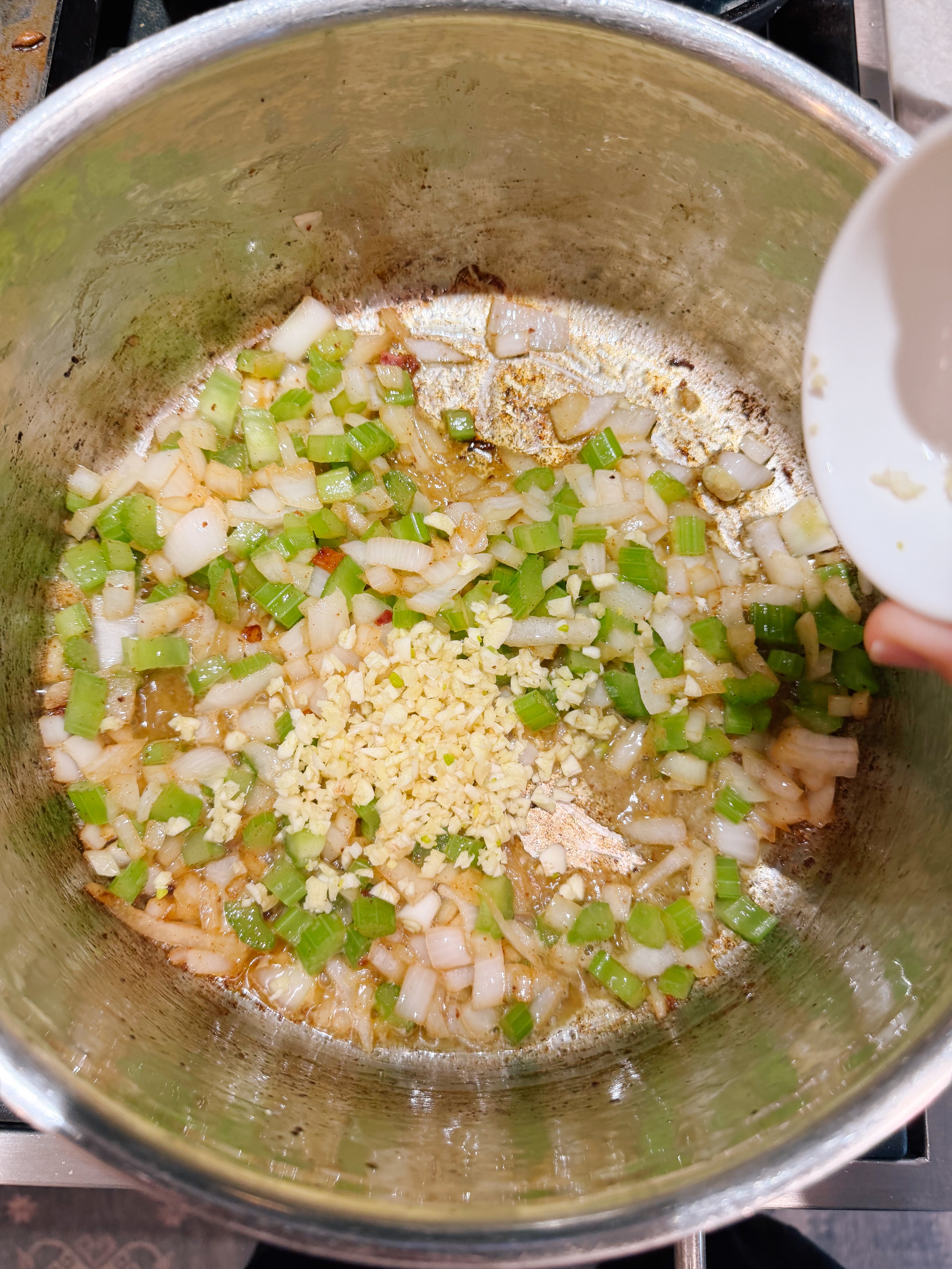 Chopped onions, celery, and minced garlic being sautéed in a pot for a cooking preparation
