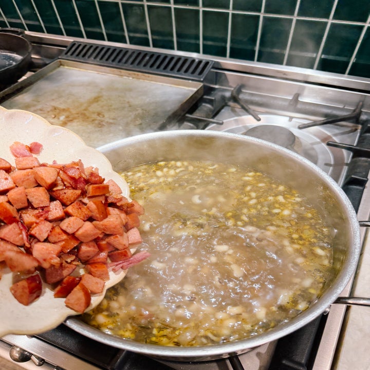 Diced sausage being added to a pot of simmering soup or stew on a stovetop
