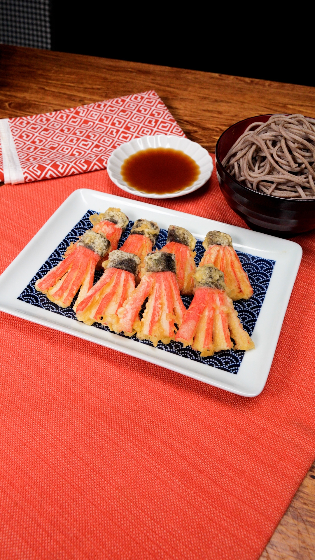 天ぷらの盛り合わせが白い皿に美しく並べられ、そば、つけ汁と共に食卓に置かれている様子。