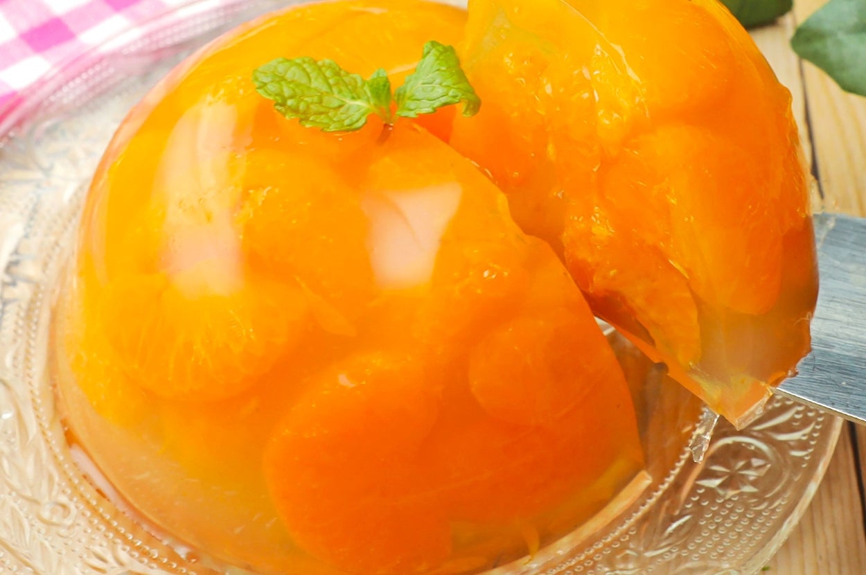 ゼリーに包まれたみかんのスライスが透明のガラス皿にのっている。上にミントの葉が飾られている。