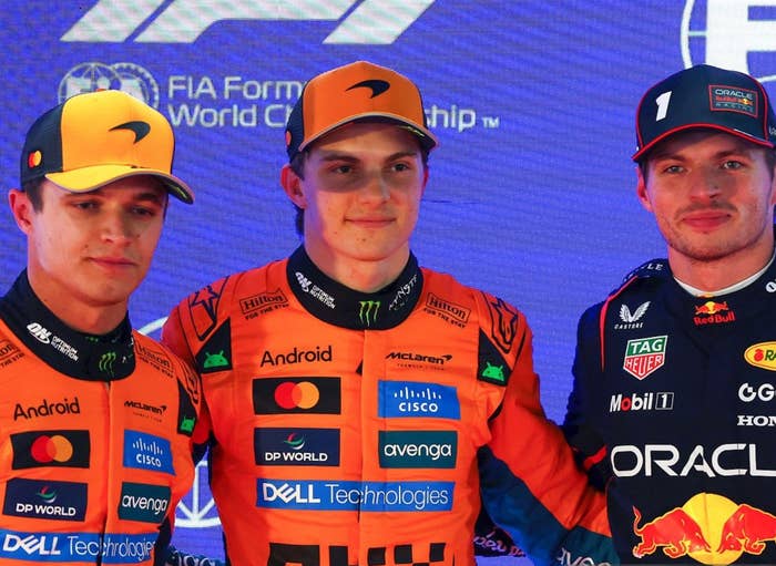 Three race car drivers in branded suits stand together at an FIA Formula 1 event