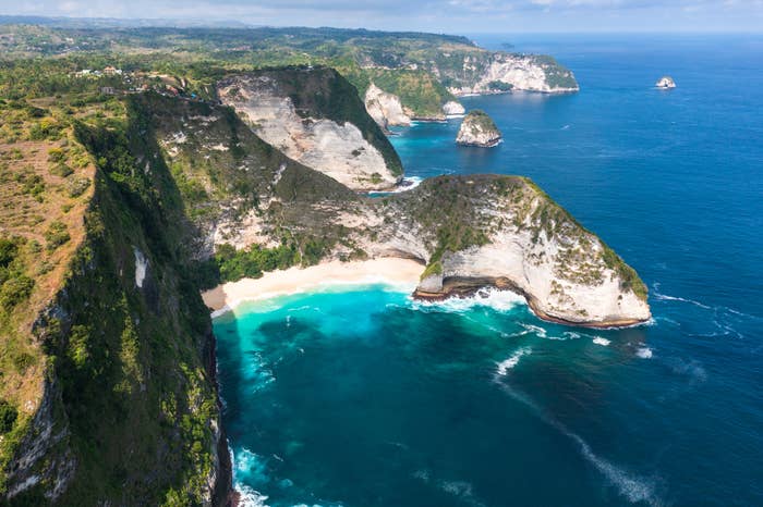 Aerial presumption    of melodramatic  coastal cliffs with turquoise waves crashing onto a secluded beach, surrounded by lush greenery