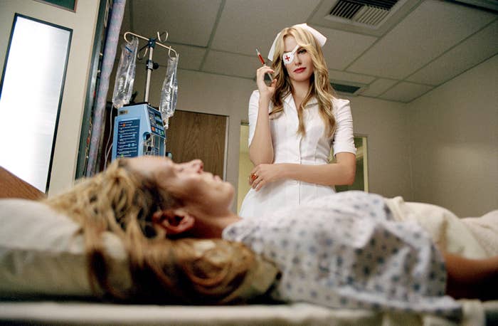 A person dressed as a nurse with a syringe stands over someone lying in a hospital bed